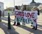 A group of people standing outside holding a sign, "God's love knows no borders"