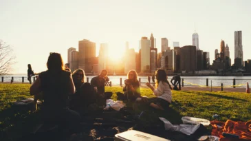 A city landscape at sunset with young adults sitting having a picnic.