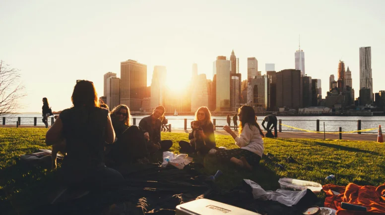 A city landscape at sunset with young adults sitting having a picnic.