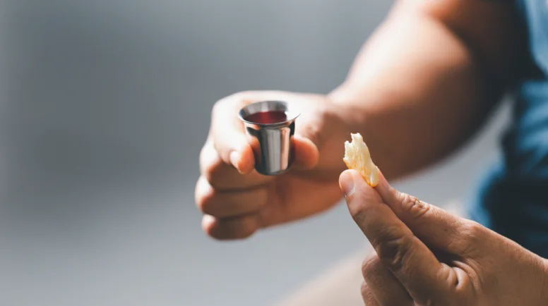 Someone holding a piece of communion bread and a cup of either grape juice or wine.
